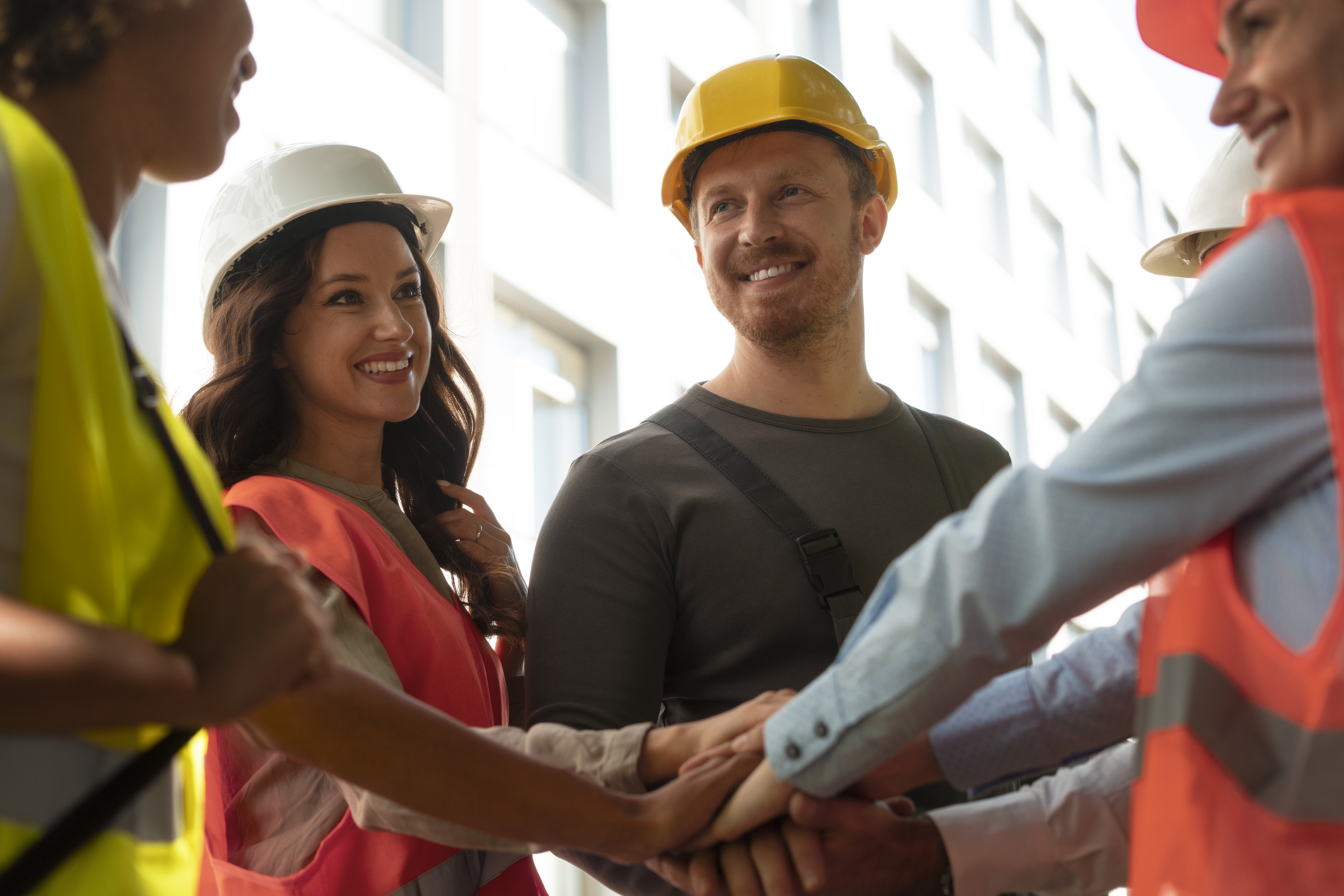 Construction team of diverse professionals in safety gear joining hands to symbolize workforce collaboration.