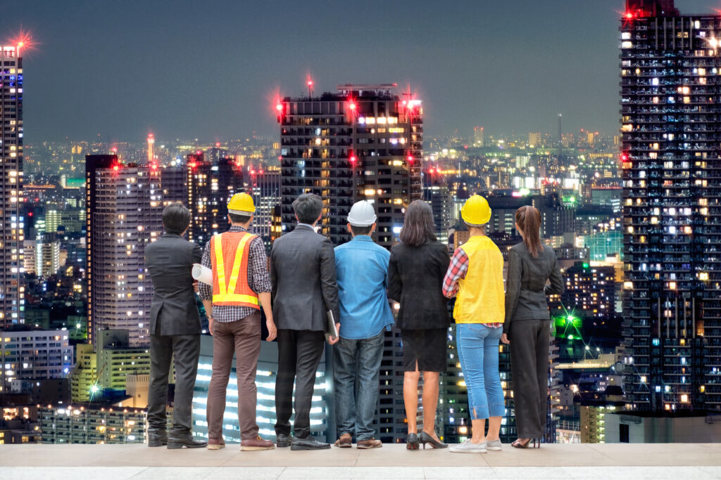 A diverse team of engineers and business professionals overlooking illuminated skyscrapers in a modern city at night.